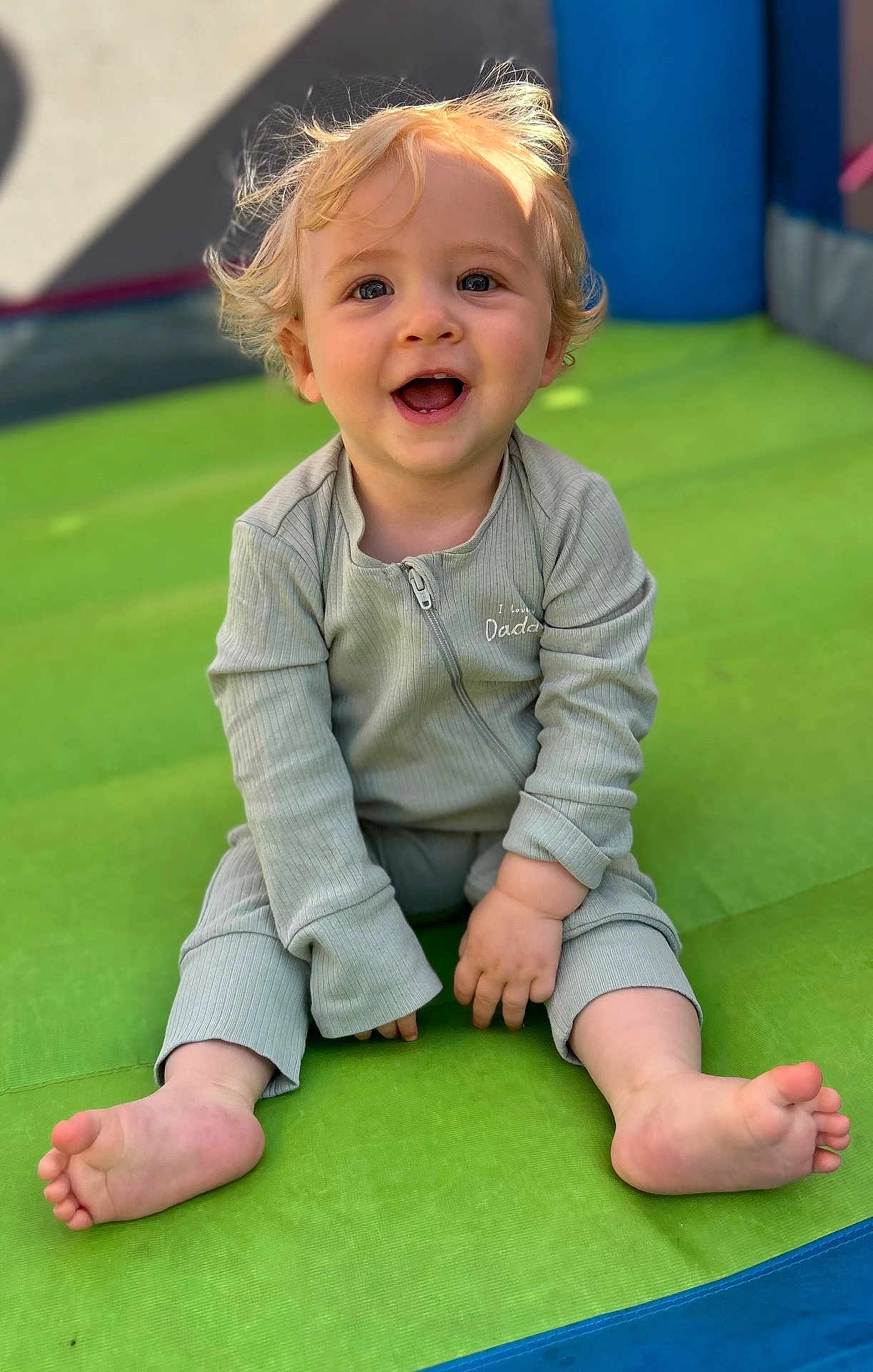 Carter joined the competition — help win amazing prizes! toddler, child, smiling, happy, blonde_hair, sitting, outdoor, playground, green_mat, barefoot, long_sleeves, casual_clothing, cute, portrait, young_child, sunlight, face, baby, one_person, infant