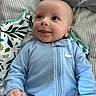 baby, infant, onesie, blue_clothing, smiling, tongue_out, lying_down, blanket, striped_sheet, face, head, cute, playful, young_child, child, person, happy, indoors, soft_lighting, nike_logo