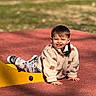 child, toddler, smiling, outdoor, playground, crawling, sunlight, jacket, pants, mickey_mouse, yellow_structure, red_surface, happy, casual_clothing, playtime, cute, daylight, person, fun, park