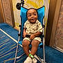 toddler, stroller, child, smiling, indoor, blue, clothing, shoes, carpet, patterned_wall, seatbelt, happy, person, footwear, baby, toy_fan, fabric, metal_frame, hand, expression