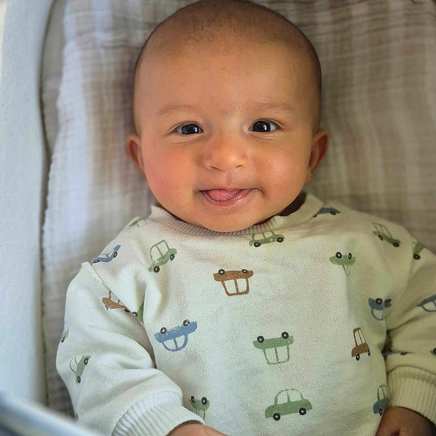 Emiliano is registered to the contest to win money with this photo: baby, infant, smiling, tongue_out, cozy, bassinet, blanket, sweater, car_prints, cute, child, portrait, indoors, happy, young_child, face, person, sleeping_area, soft, playful