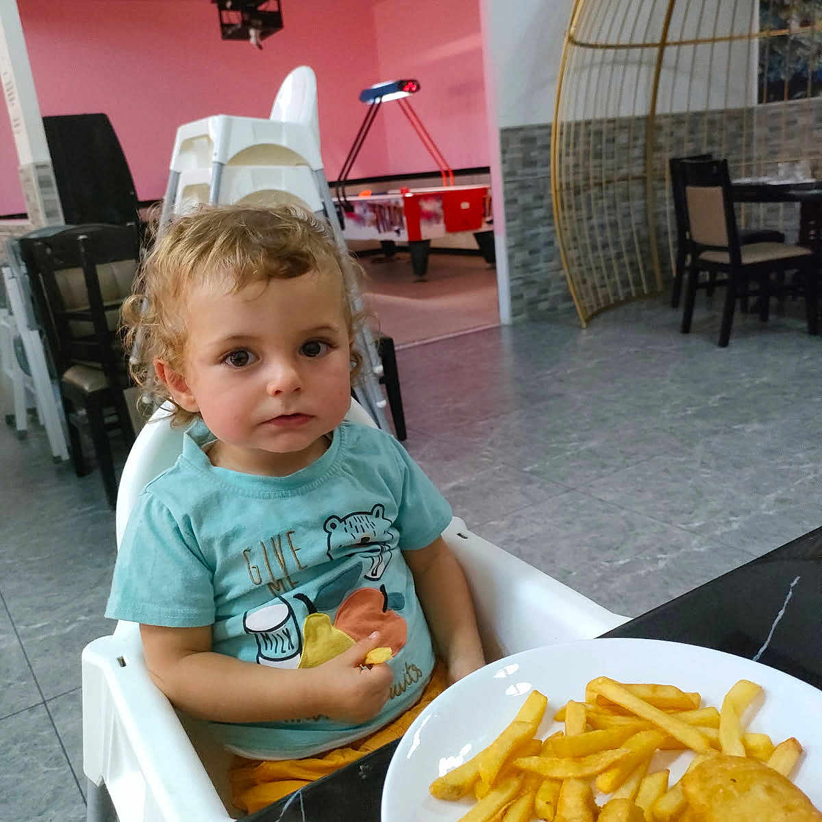 Francis participe au concours pour gagner de l'argent avec cette photo : blue_shirt, casual_clothing, chair, child, curly_hair, dining_area, floor, food, foosball_table, french_fries, high_chair, indoor, looking, modern_interior, nuggets, person, plate, table, toddler, yellow_pants