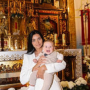David joined the competition — help win amazing prizes! altar, baby, candles, celebration, child, church, decorative, event, flowers, formal, gold, happy, holding, indoor, person, portrait, religious, smile, white_clothing, woman