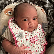 Nala joined the competition — help win amazing prizes! baby, infant, bib, face, hand, cushion, bear_pattern, clothing, striped_shirt, blanket, indoor, closeup, portrait, child, cute, expression, person, skin, head, newborn