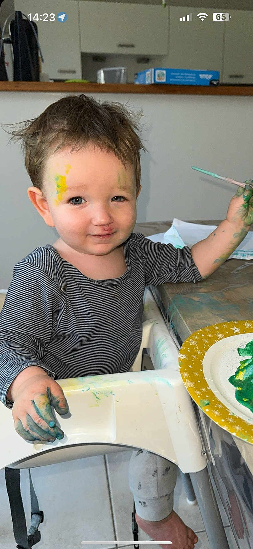 Ethan participe au concours pour gagner de l'argent avec cette photo : toddler, child, paint, messy, high_chair, face_paint, paintbrush, hand_paint, smile, striped_shirt, indoor, table, plate, foot, floor, hair, expression, art, creative, play