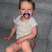 Ethan participe au concours pour gagner de l'argent avec cette photo : toddler, child, pacifier, sitting, couch, indoor, home, smile, white_clothing, infant, furniture, living_room, cute, baby, person, young_child, relaxing, face, skin, legs