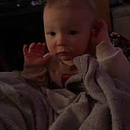 Desiree joined the competition — help win amazing prizes! baby, blanket, child, indoor, television, screen, person, face, hands, sweater, furniture, living_room, soft_texture, cozy, expression, couch, home, curly_hair, young_child, dim_light