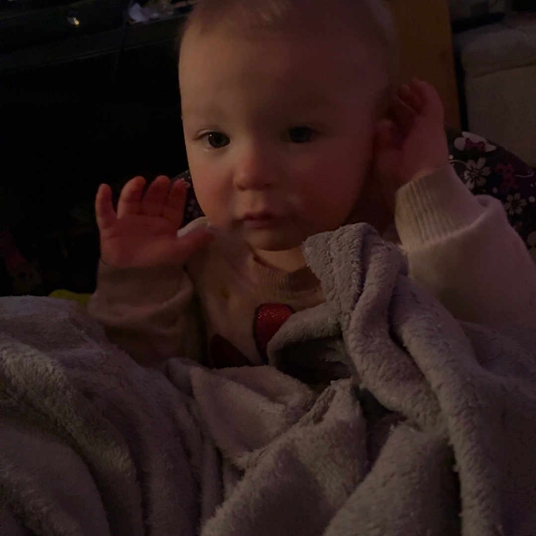 Desiree joined the competition — help win amazing prizes! baby, blanket, child, couch, cozy, curly_hair, dim_light, expression, face, furniture, hands, home, indoor, living_room, person, screen, soft_texture, sweater, television, young_child