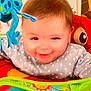 baby, smile, face, toy, blue_elephant, red_toy, infant, clothing, stars_pattern, play_area, child, happy, cute, indoor, colorful, plastic_toy, activity_center, closeup, cheerful, young_child