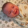 baby, smiling, face, infant, clothing, pattern, animal_print, star_pattern, changing_pad, happy, cute, lying_down, skin, head, eyes, mouth, cheeks, indoors, child, person
