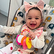 Nova joined the competition — help win amazing prizes! baby, child, smiling, headband, pink_bow, toy, baby_chair, elephant_pattern, happy, indoor, clothing, white_shirt, floral_pants, infant, cute, playful, seated, colorful, portrait, young_child
