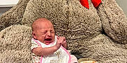 Haizley joined the competition — help win amazing prizes! baby, infant, crying, bib, plush_toy, teddy_bear, red_bow, blanket, indoor, person, newborn, cute, soft_toy, child, furniture, cozy, pink_clothing, head, sitting, expression
