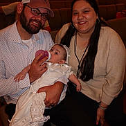Everleigh joined the competition — help win amazing prizes! baby, bottle, feeding, family, man, woman, smiling, glasses, hat, long_hair, beard, white_clothing, seated, indoor, ceremony, people, jewelry, happy, portrait, infant