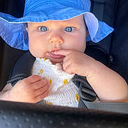 Atlas is registered to the contest to win money with this photo: baby, blue_hat, child, curious, face, hand, infant, outdoor, people, portrait, seatbelt, stroller, sunhat, young_child, white_clothing, yellow_flower_pattern, closeup, skin, expression, bright_eyes