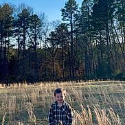 Augustus joined the competition — help win amazing prizes! child, boy, field, grass, trees, plaid_shirt, jeans, outdoor, nature, sunlight, sky, smile, standing, rural, daytime, young_child, casual_clothing, happy, forest, tall_grass
