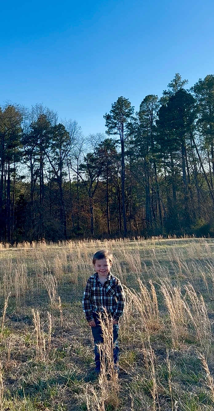 Augustus joined the competition — help win amazing prizes! child, boy, field, grass, trees, plaid_shirt, jeans, outdoor, nature, sunlight, sky, smile, standing, rural, daytime, young_child, casual_clothing, happy, forest, tall_grass