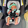 baby, infant, car_seat, pacifier, headband, black, mint_green, clothing, newborn, sitting, safety_harness, indoors, floor, wood_floor, cute, person, child, infant_fashion, toddler, baby_accessory