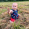baby, child, grass, field, outdoor, nature, trees, greenery, curious, sitting, summer, casual_clothing, star_pattern, red_shorts, blue_top, infant, person, cute, daylight, smiling