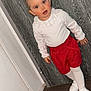 child, toddler, portrait, standing, indoor, red_shorts, white_top, white_tights, white_shoes, hair_buns, red_eyes, wooden_wall, door, floor, curious_expression, blush_cheeks, flash_photography, fashion, close_up, cute