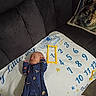 baby, infant, onesie, blanket, milestone_blanket, numbers, stars, couch, pillow, wolf_pillow, sleeping, indoors, clothing, text, soft_furnishing, carpet, peaceful, child, newborn, resting