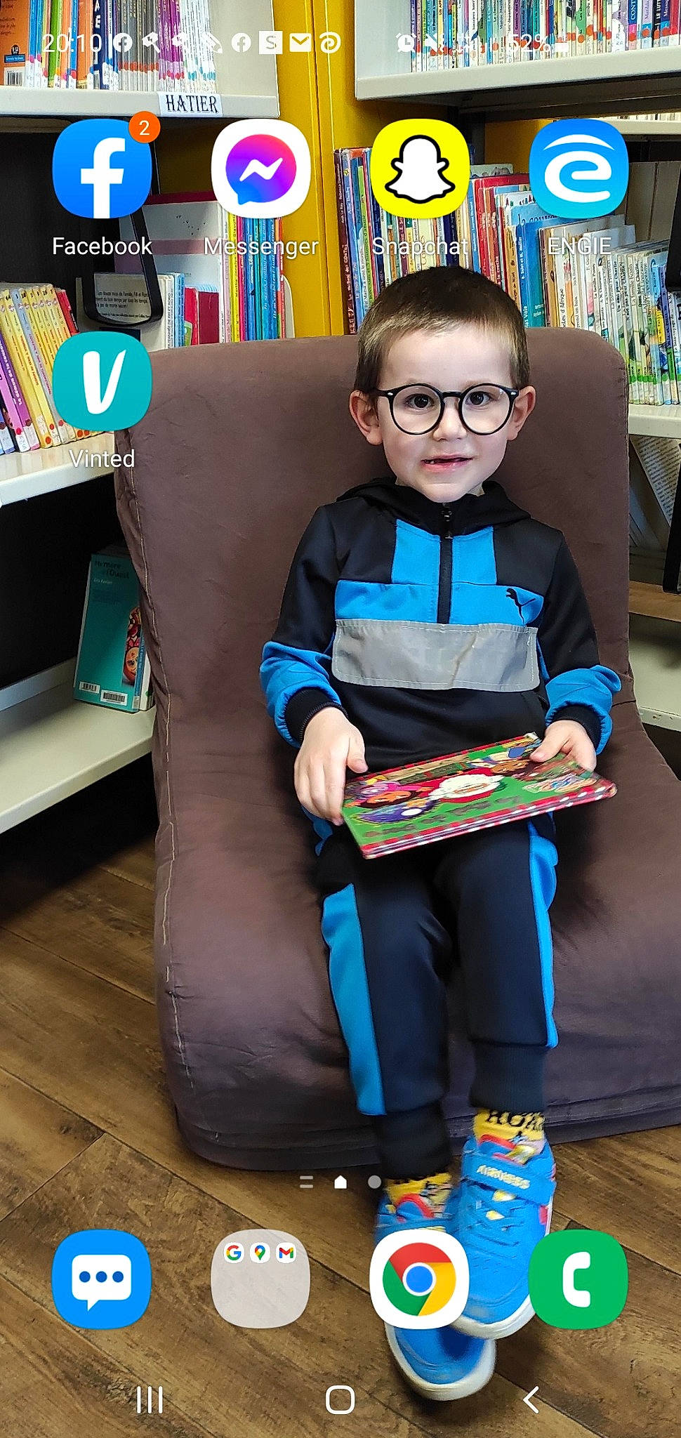 Noham participe au concours pour gagner de l'argent avec cette photo : book, bookcase, child, electric_blue, event, eyewear, fun, glasses, lap, person, play, publication, reading, room, shelf, shelving, sitting, smile, standing, t_shirt
