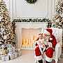 baby, candle, celebration, christmas_tree, decoration, festive, fireplace, floor, gift, holiday, indoor, pacifier, red_clothing, santa_claus, smile, stuffed_toy, wall, white_armchair, winter, wreath