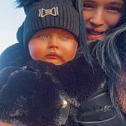 Maizey-May is registered to the contest to win money with this photo: baby, black_coat, blue_eyes, child, coat, daylight, face, fur_coat, hand, hat, holding, long_hair, outdoor, pink_pants, pom_pom, portrait, smile, warm_clothing, winter_clothing, woman