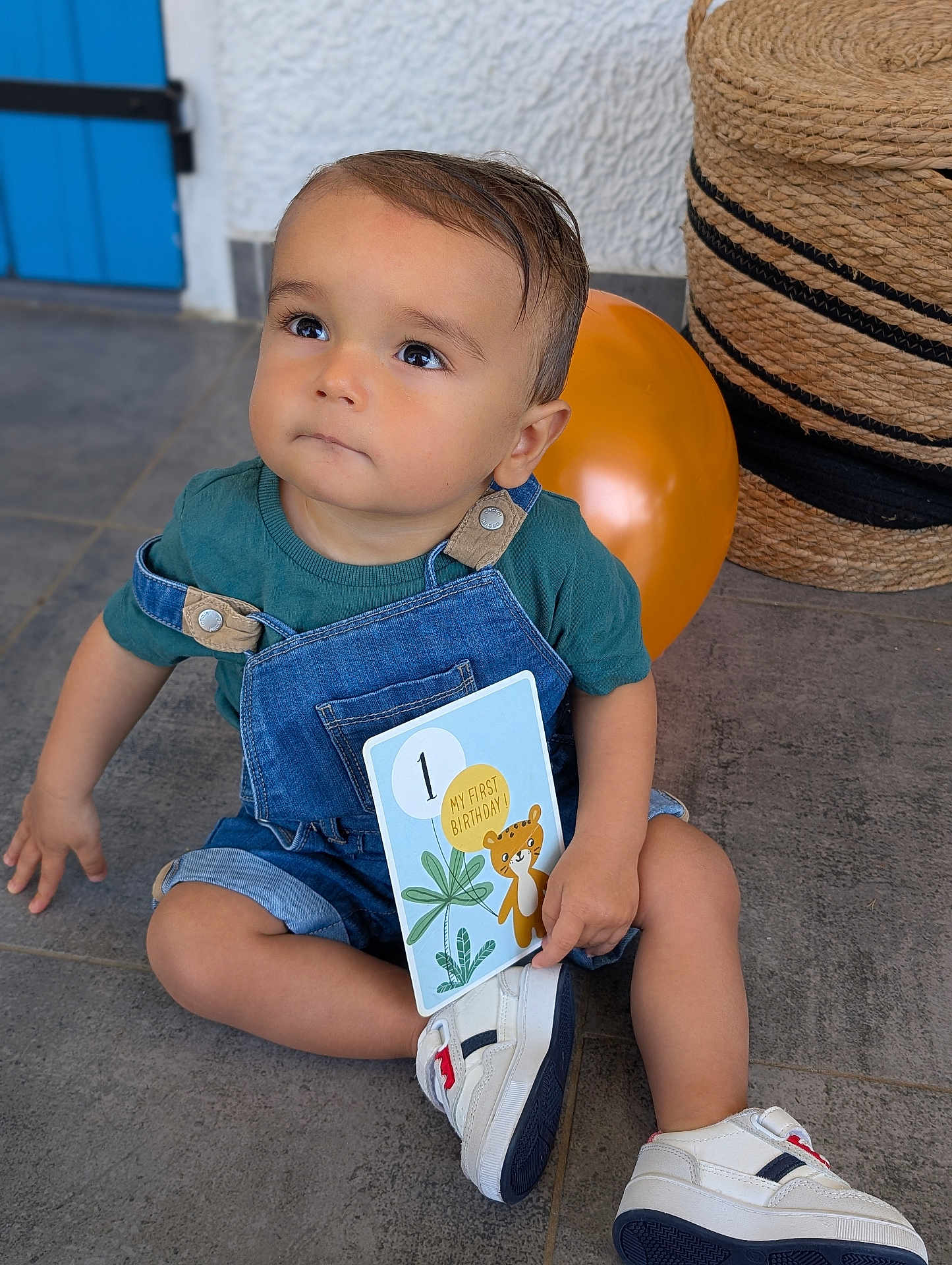 Lisandro participe au concours pour gagner de l'argent avec cette photo : toddler, child, birthday, denim_overalls, sneakers, balloon, card, floor, indoor, blue_shirt, cute, curious, seated, woven_basket, celebration, portrait, baby, one_year_old, happy, casual_clothing