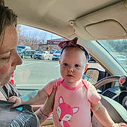 Maria is registered to the contest to win money with this photo: baby, child, woman, car_interior, car_window, parking_lot, sunlight, headband, pink_clothing, fox_design, adult, person, seat, steering_wheel, hand, bracelet, daylight, vehicle, window, outdoor