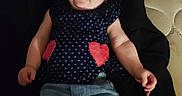 Maria is registered to the contest to win money with this photo: baby, child, infant, face, person, clothing, shirt, hearts, blue, jeans, denim, sitting, cute, chubby, indoor, fabric, mattress, pile_of_clothes, casual, portrait