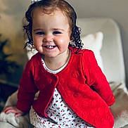 Alba a rejoint le concours — aidez-le/la à gagner de superbes lots ! toddler, child, smiling, red_cardigan, curly_hair, bow, dress, white_tights, chair, indoor, portrait, happy, cute, baby, seated, cozy, person, face, young, fashion