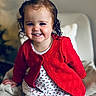 toddler, child, smiling, red_cardigan, curly_hair, bow, dress, white_tights, chair, indoor, portrait, happy, cute, baby, seated, cozy, person, face, young, fashion