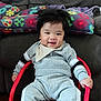 baby, child, smiling, indoor, sitting, clothing, bib, socks, chair, red, grey, face, happy, furniture, couch, pillow, patterned, person, cozy, portrait