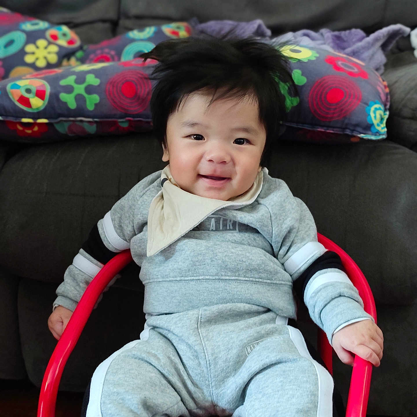 Eiji participe au concours pour gagner de l'argent avec cette photo : baby, bib, chair, child, clothing, couch, cozy, face, furniture, grey, happy, indoor, patterned, person, pillow, portrait, red, sitting, smiling, socks