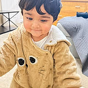 Azlan is registered to the contest to win money with this photo: toddler, child, onesie, fuzzy_clothing, animal_costume, indoor, living_room, carpet, furniture, wooden_cabinet, curly_hair, cute, baby, person, smiling, young_child, cozy, soft_lighting, home, playful