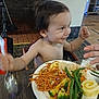 Rey is registered to the contest to win money with this photo: toddler, child, food, plate, noodles, rice, vegetables, broccoli, green_beans, cake, spoon, table, indoor, highchair, person, smile, happy, meal, dining, fork