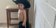 Rey joined the competition — help win amazing prizes! toddler, child, boy, hat, cowboy_hat, shirtless, shorts, sneakers, indoor, floor, chair, wall, smile, standing, looking_at_camera, wood_floor, white_wall, casual, playful, small_person