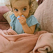 Irina participe au concours pour gagner de l'argent avec cette photo : child, toddler, baby, pacifier, blanket, pink_blanket, couch, pillow, blue_dress, topknot, hair_tie, curly_hair, big_eyes, hand, portrait, indoors, cozy, cute, looking_sideways, soft_texture