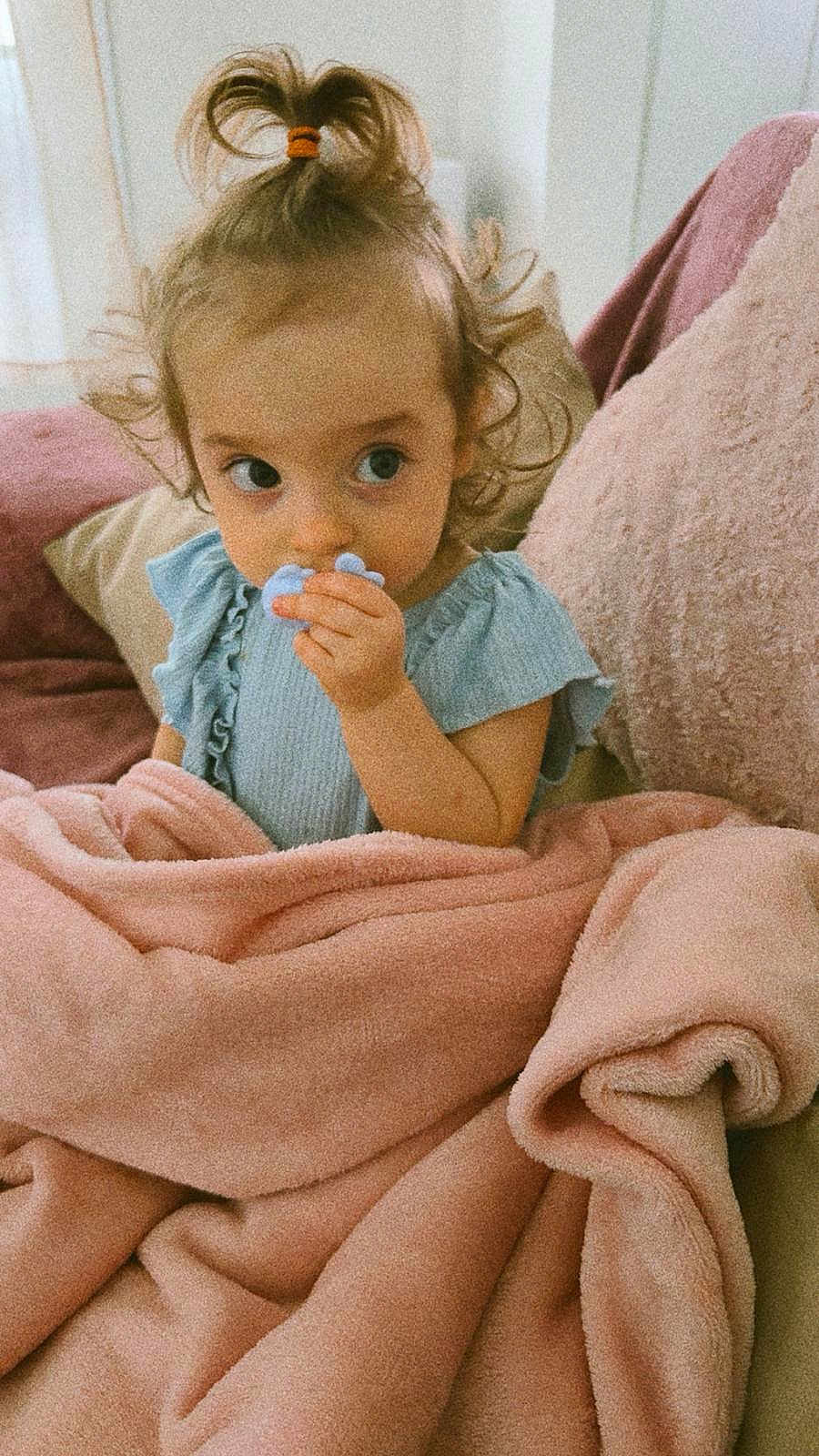 Irina participe au concours pour gagner de l'argent avec cette photo : child, toddler, baby, pacifier, blanket, pink_blanket, couch, pillow, blue_dress, topknot, hair_tie, curly_hair, big_eyes, hand, portrait, indoors, cozy, cute, looking_sideways, soft_texture