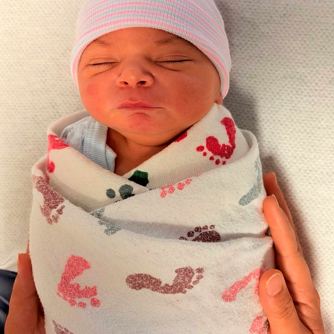 Ibrahim joined the competition — help win amazing prizes! newborn, baby, sleeping, infant, portrait, face, eyes_closed, knit_hat, beanie, swaddled, blanket, textile, hands, caregiver, indoors, close_up, peaceful, resting, pink, cozy