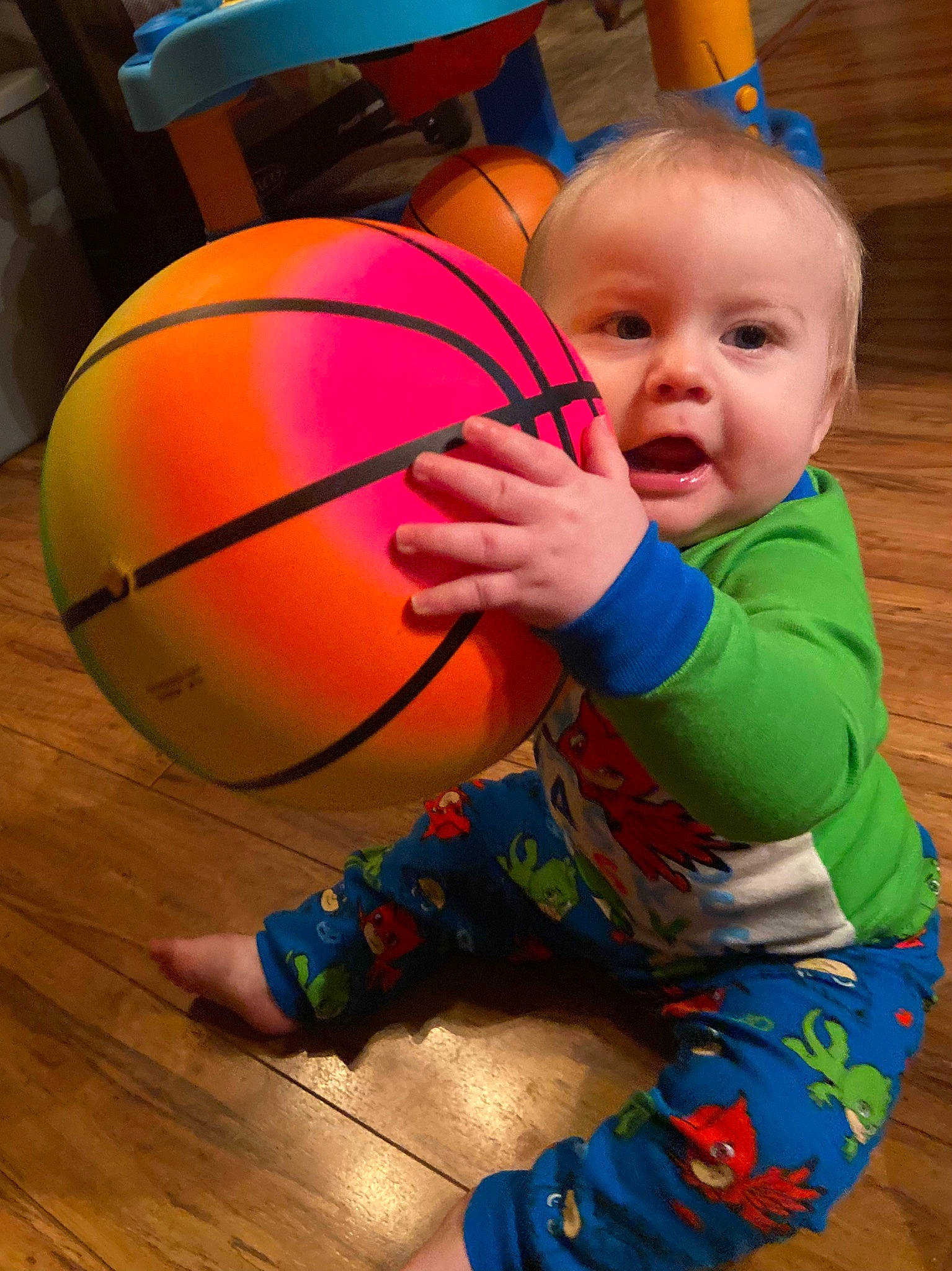 Brodie is registered to the contest to win money with this photo: baby, baby_toddler_clothing, ball, ball_game, basketball, blue, child, facial_expression, flooring, fun, happy, leisure, orange, person, smile, sports_equipment, sports_toy, toddler, wood, yellow