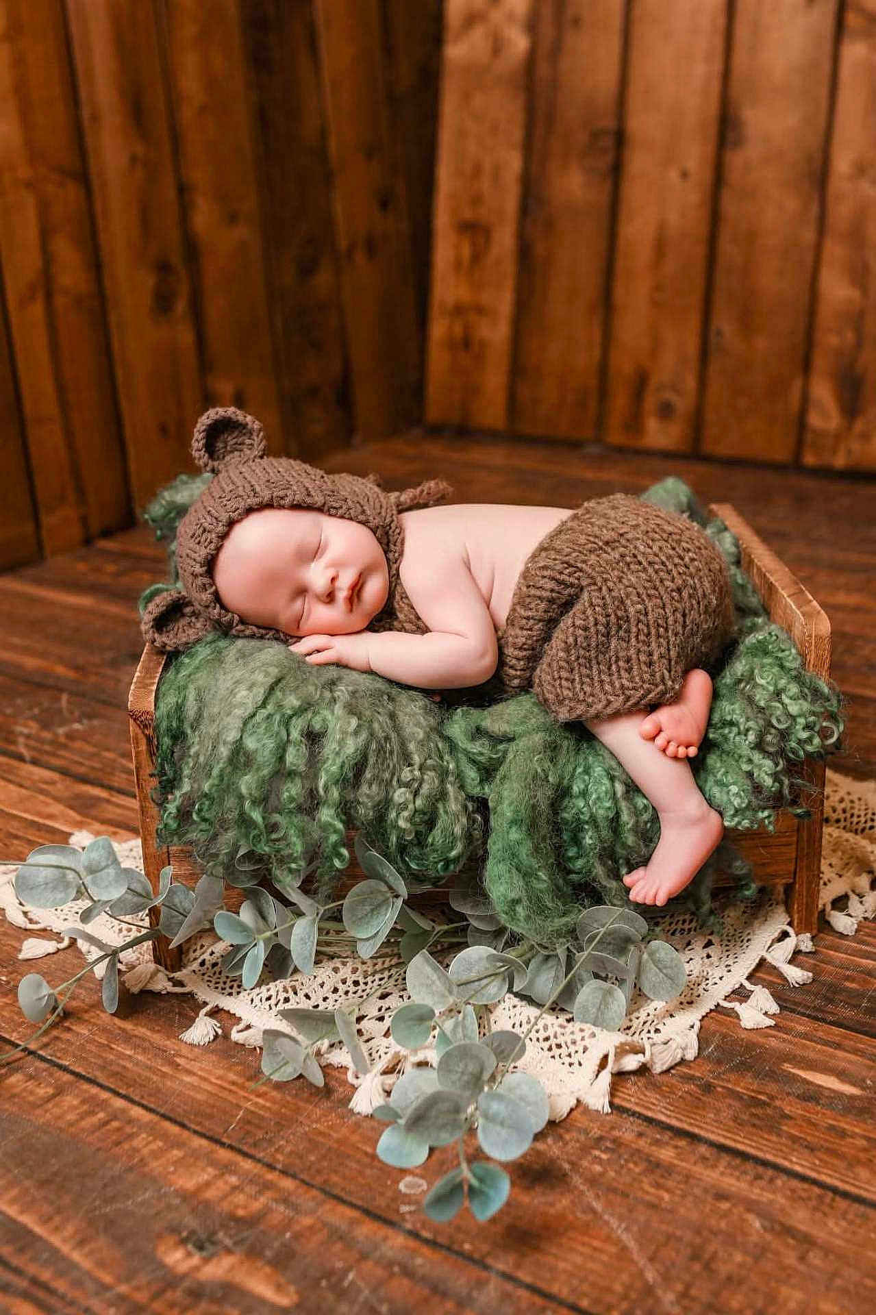 Hugo joined the competition — help win amazing prizes! baby, sleeping, knitted_hat, knitted_pants, wooden_bed, green_blanket, fluffy_texture, rustic, wooden_floor, wooden_wall, eucalyptus_leaves, lace_doily, peaceful, infant, cute, cozy, portrait, indoors, newborn, soft_lighting