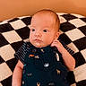 baby, infant, child, portrait, clothing, blue_overall, striped_shirt, animal_print, blanket, checkered_pattern, face, hand, eyes, skin, expression, indoors, soft_texture, orange_background, newborn, cute