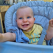 Axel a rejoint le concours — aidez-le/la à gagner de superbes lots ! baby, child, blue_eyes, high_chair, smiling, outdoor, seat_belt, gray_cushion, yellow_tshirt, reaching_hand, face, portrait, happy, infant, person, chair, daylight, casual_clothing, wooden_table, plastic_chair