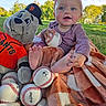 baby, infant, child, smiling, outdoor, park, baseball, sports, plush_toy, dog_toy, blanket, pink_headband, pink_clothing, sitting, bare_feet, green_grass, trees, sunlight, portrait, happy