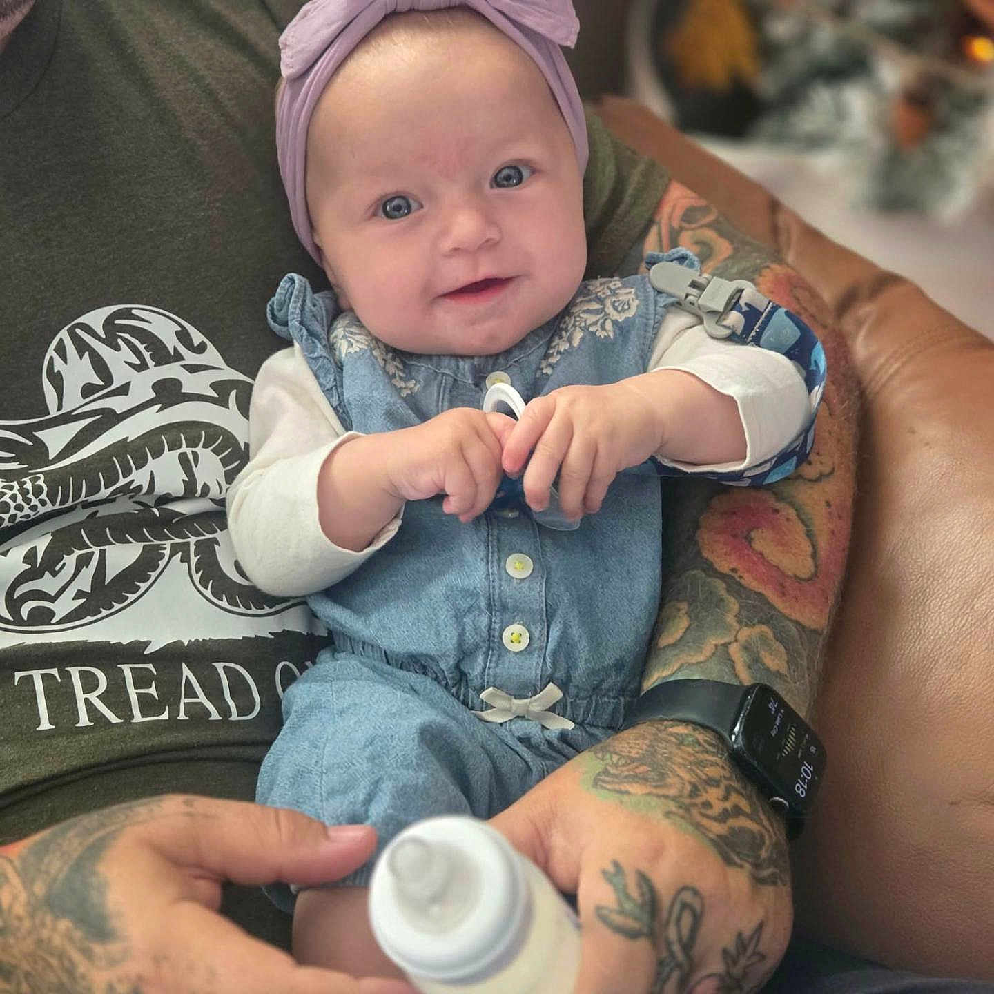 Ava joined the competition — help win amazing prizes! baby, infant, child, portrait, smiling, headband, lavender, denim, overalls, bottle, feeding, adult, tattoos, arms, hands, couch, christmas_tree, indoors, festive, family