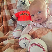 Ava is registered to the contest to win money with this photo: baby, infant, smiling, portrait, baseball, softball, plush_toy, mascot, sports, san_francisco_giants, cap, blanket, bed, indoors, pink_clothing, happy, blue_eyes, toys, close_up, family_photo