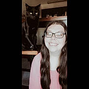 Binx is registered to the contest to win money with this photo: woman, cat, black_cat, glasses, smiling, long_hair, indoor, chair, person, pet, furniture, happy, portrait, home, casual, seated, cute, animal, friendship, light