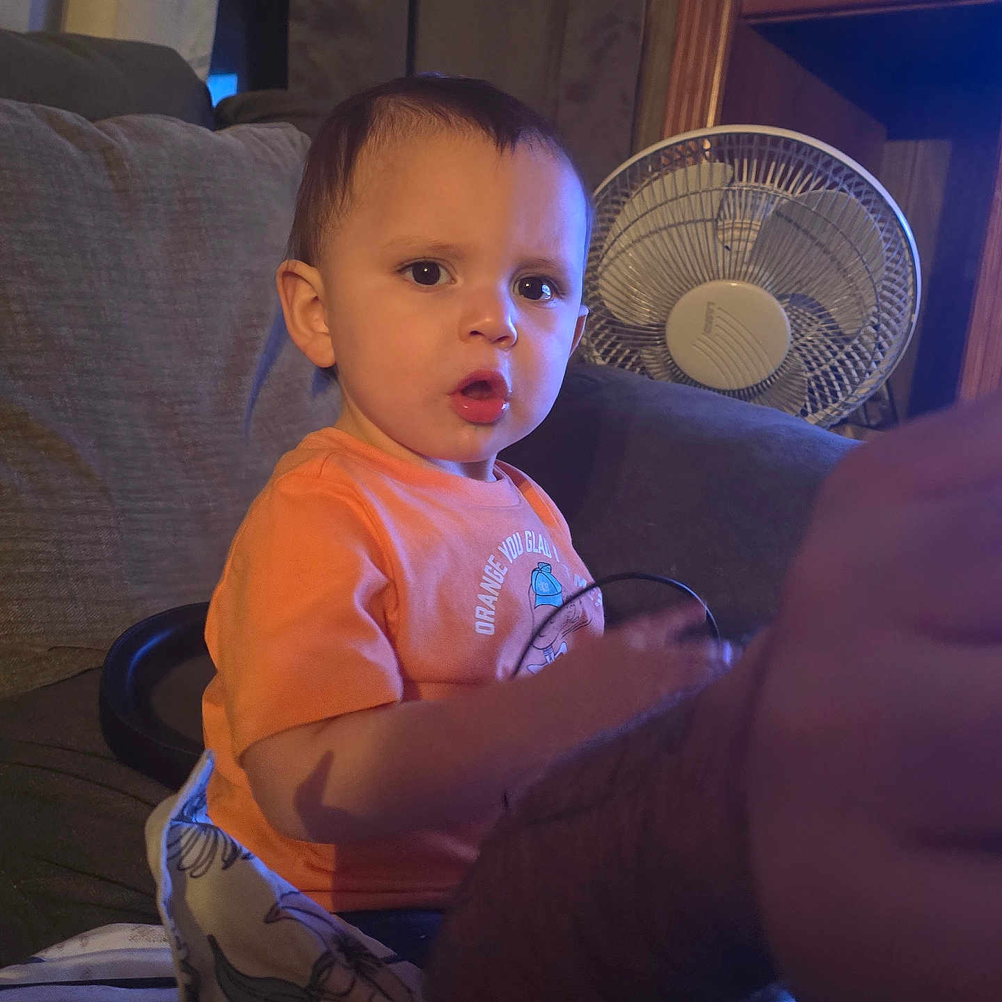 Abel joined the competition — help win amazing prizes! adult_arm, arm, blanket, cable, candid, child, couch, curtain, face, fan, furniture, indoor, living_room, night_light, orange_shirt, portrait, sitting, sofa, surprised_expression, toddler