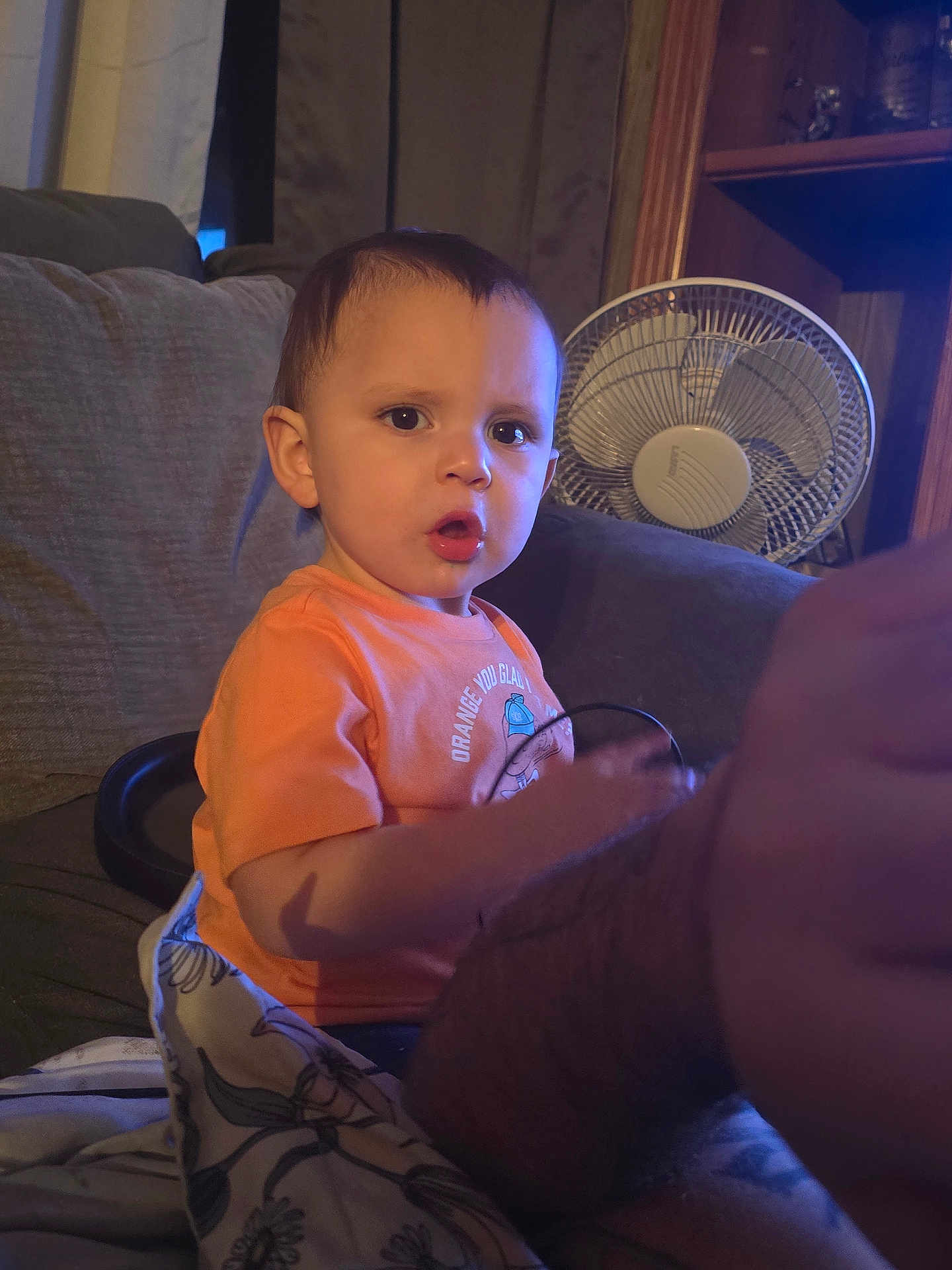 Abel joined the competition — help win amazing prizes! child, toddler, surprised_expression, orange_shirt, couch, sofa, living_room, fan, blanket, arm, adult_arm, cable, portrait, indoor, night_light, curtain, furniture, sitting, candid, face